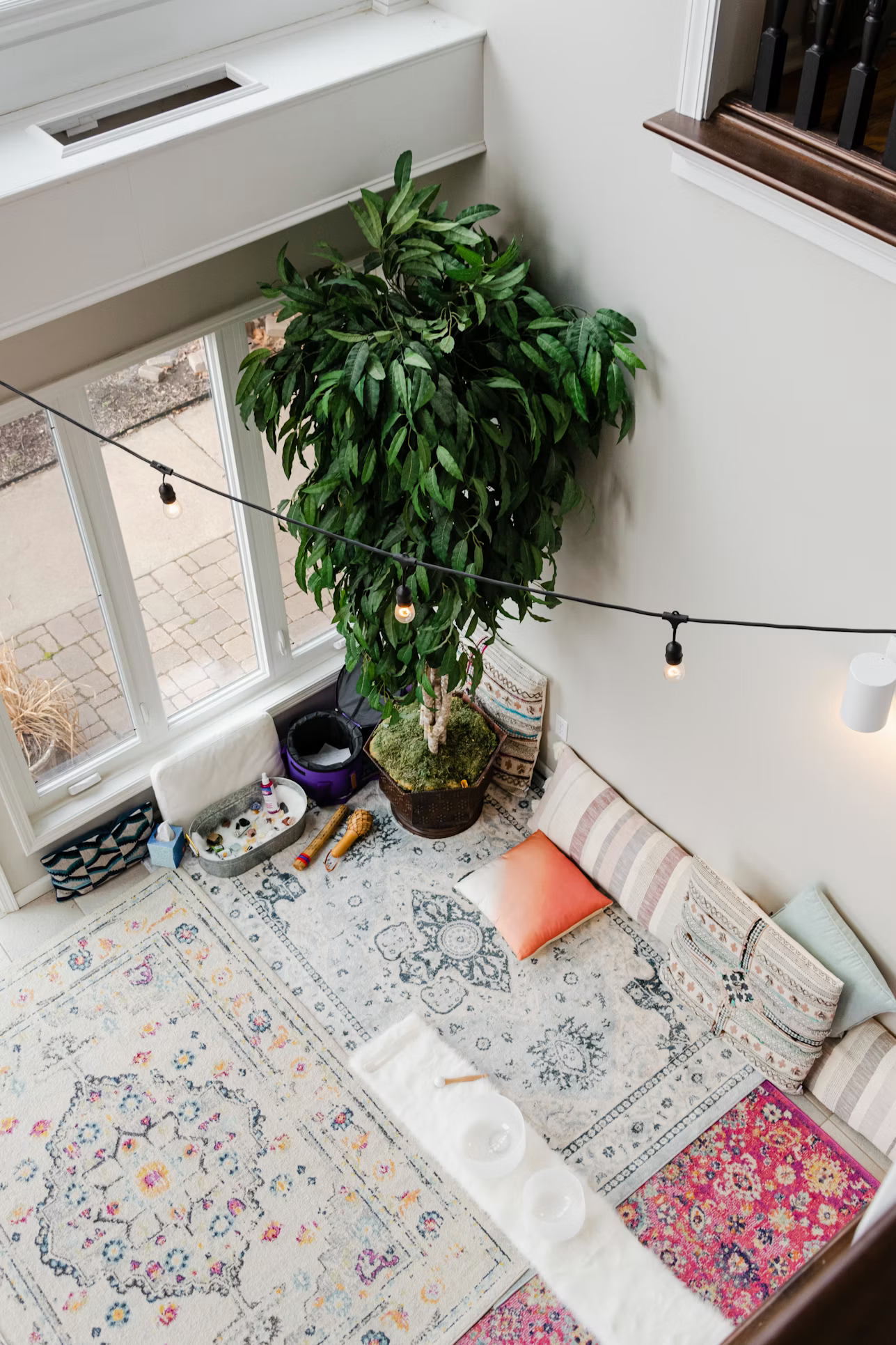 Yoga studio seen from above with a large green plant, rugs, cushions and string lights